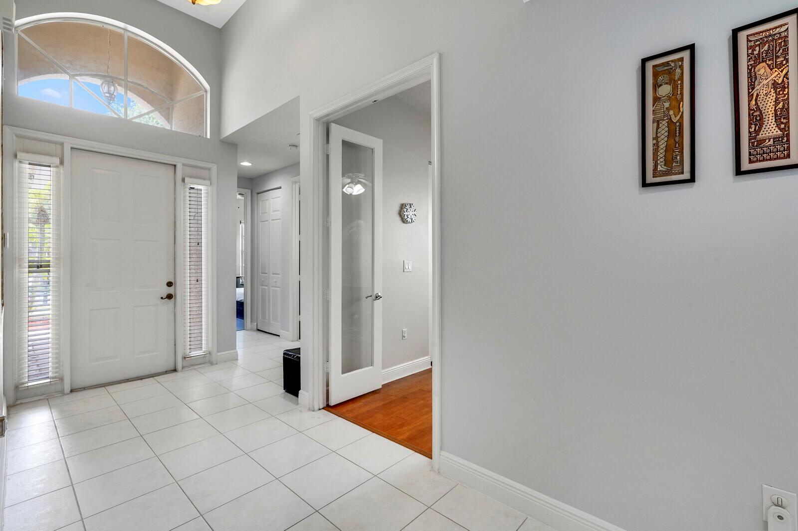 A bright entryway with white tile flooring, a glass-paneled door, and Egyptian-style wall art — 19084 Skyridge Circle, Boca Raton FL 33498, BOCA RATON, FL