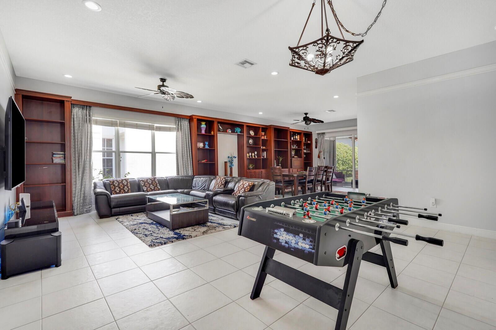 A spacious living room features a foosball table, leather sectional, and built-in wooden shelving — 19084 Skyridge Circle, Boca Raton FL 33498, BOCA RATON, FL
