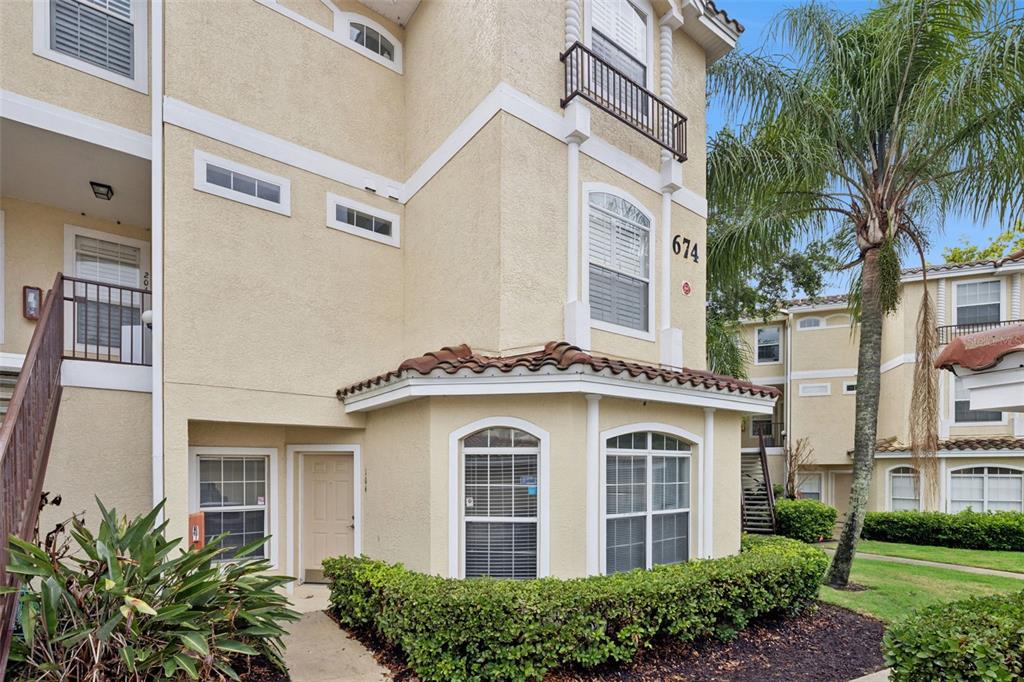 A three-story tan stucco apartment building features arched windows, a tiled roof, and landscaping — 674 SANDY NECK LANE UNIT 104, ALTAMONTE SPRINGS, FL