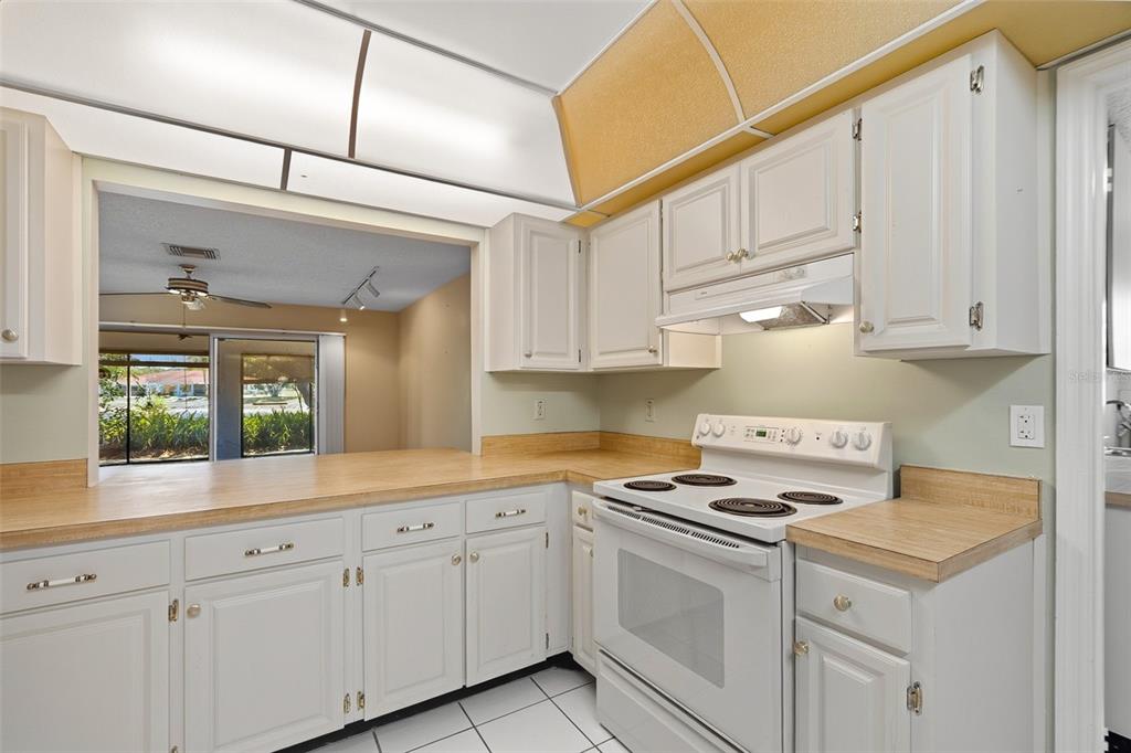 A kitchen with white cabinets, light wood countertops, a white electric stove, and tile flooring — 1027 BLUEWATER DRIVE, SUN CITY CENTER, FL