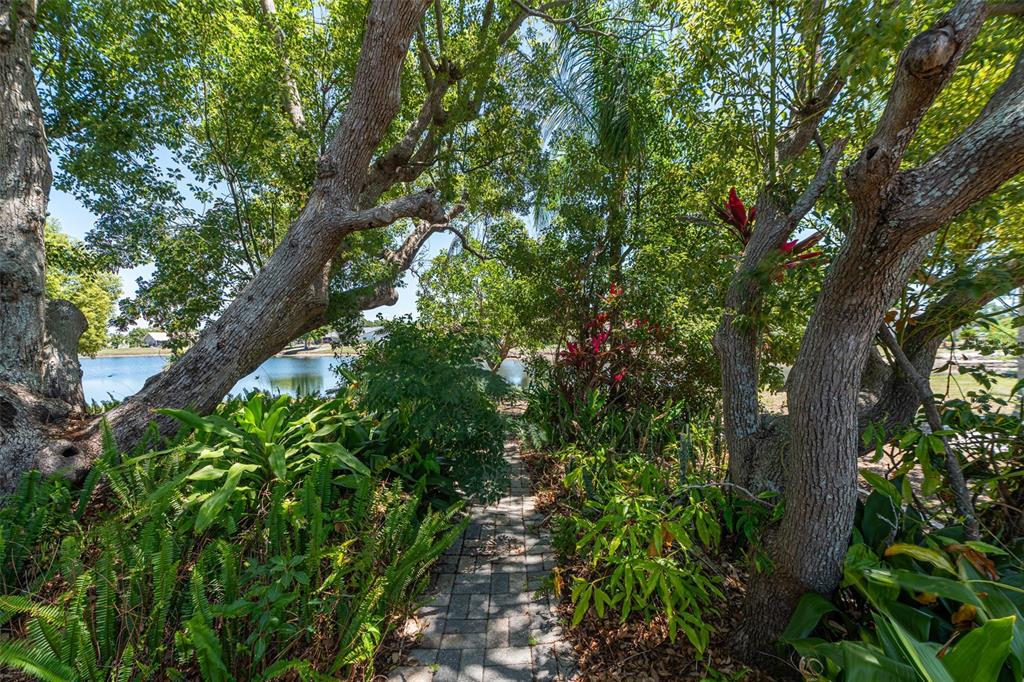 A stone path leads through a lush, tree-lined garden toward a view of a lake — 1027 BLUEWATER DRIVE, SUN CITY CENTER, FL