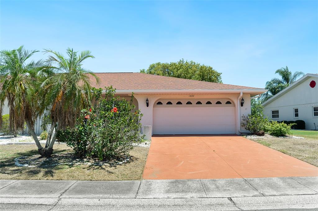 A single-story house with a pink exterior, a two-car garage, and a palm tree — 1027 BLUEWATER DRIVE, SUN CITY CENTER, FL
