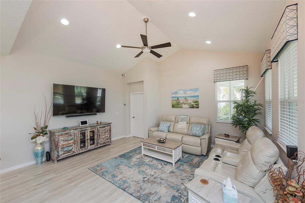 A living room features a vaulted ceiling, light wood flooring, a television, and neutral furniture — 572 LANDSHARK BOULEVARD, DAYTONA BEACH, FL