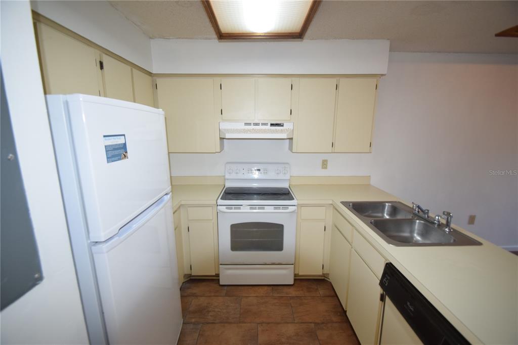 A kitchen features light yellow cabinets, white appliances, a double sink, and brown tile flooring — 6055 TOPHER TRAIL UNIT 6055, MULBERRY, FL