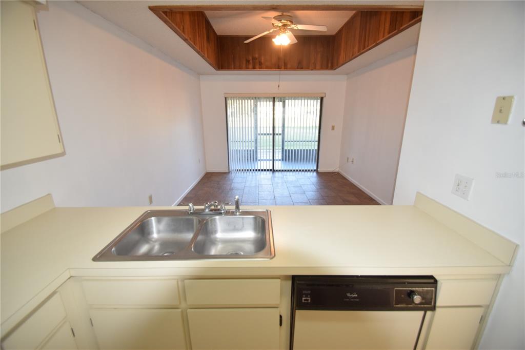 A kitchen sink and dishwasher overlook a dining area with a tray ceiling and sliding doors — 6055 TOPHER TRAIL UNIT 6055, MULBERRY, FL