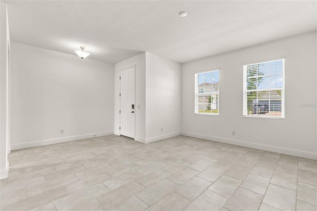An empty room with light-colored tile flooring, white walls, two windows, and a white door — 1863 CHURCH LAKE STREET, GROVELAND, FL