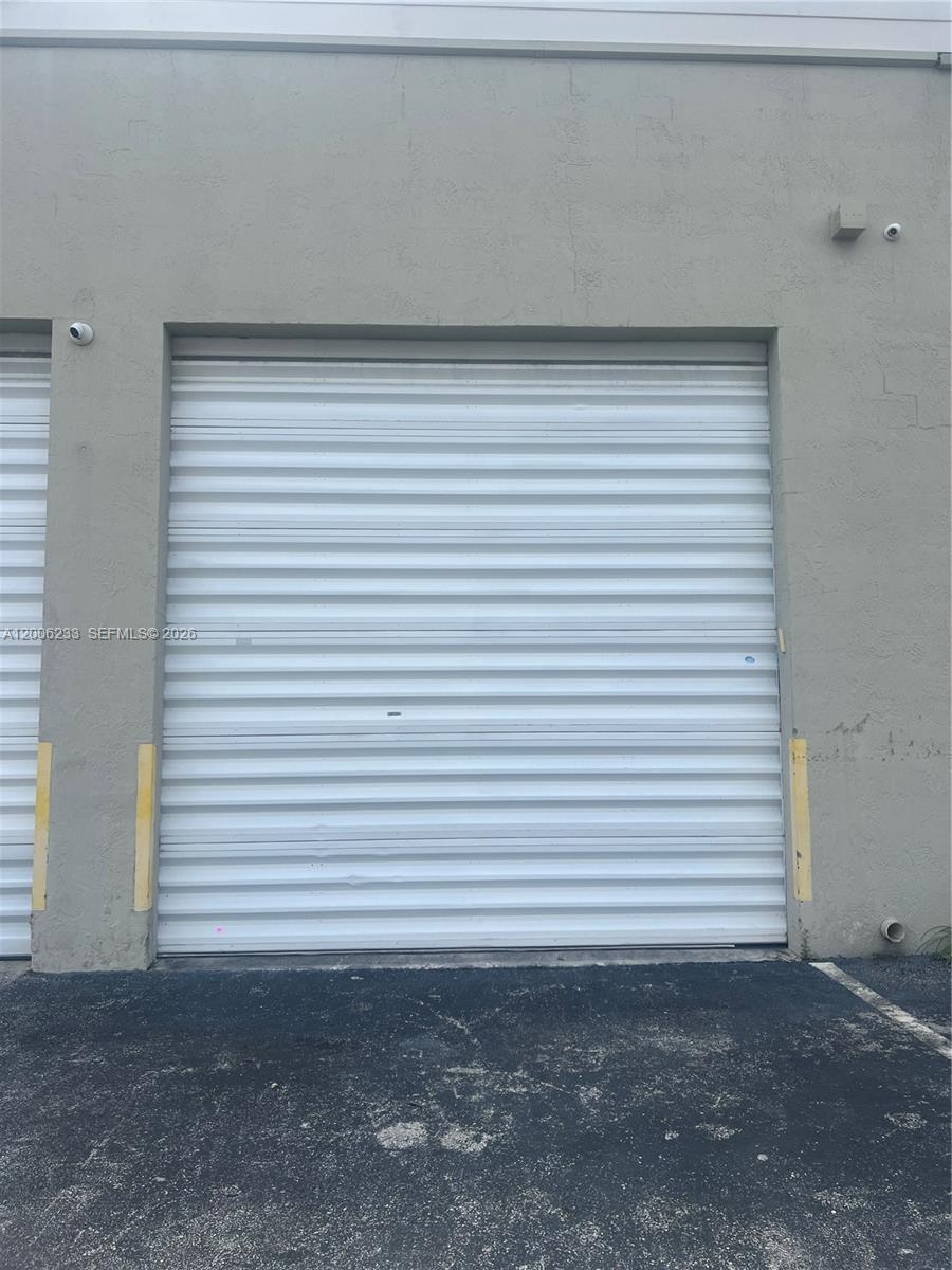 A closed white metal roll-up garage door is set into a gray concrete exterior wall — 11467 NW 34th St # 11471, Doral FL 33178, DORAL, FL