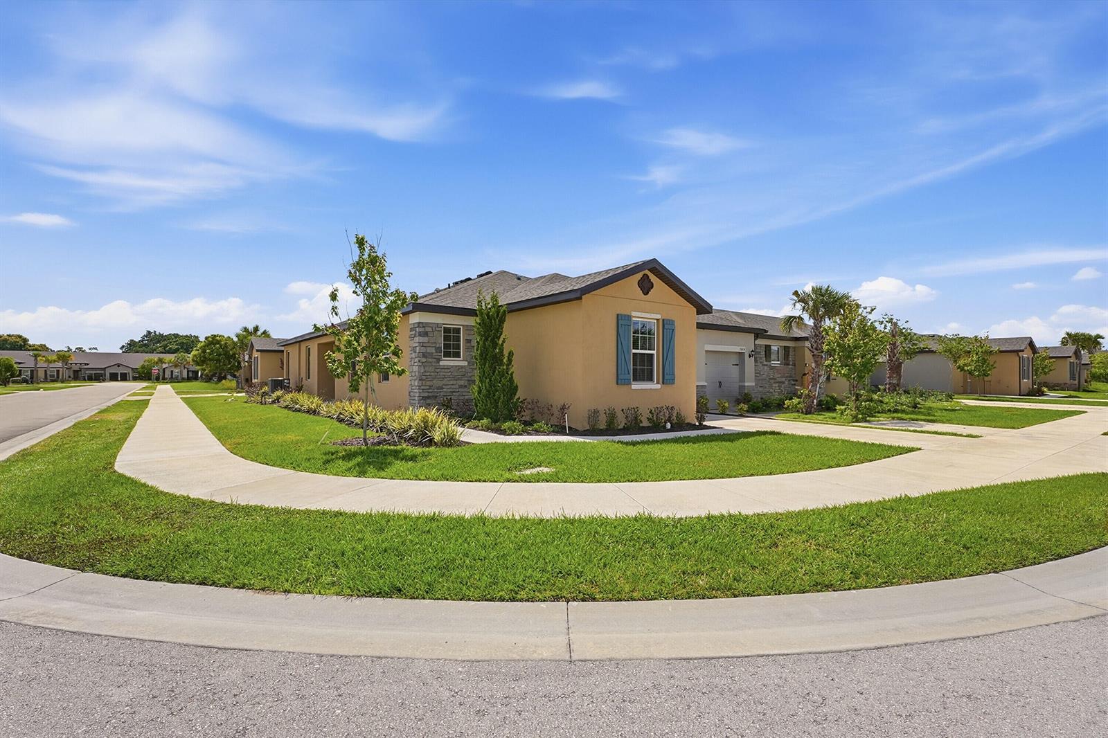 A tan, single-story suburban house with stone accents and blue shutters sits on a corner lot — 1802 Celebration Drive, Fort Pierce FL 34947, FORT PIERCE, FL