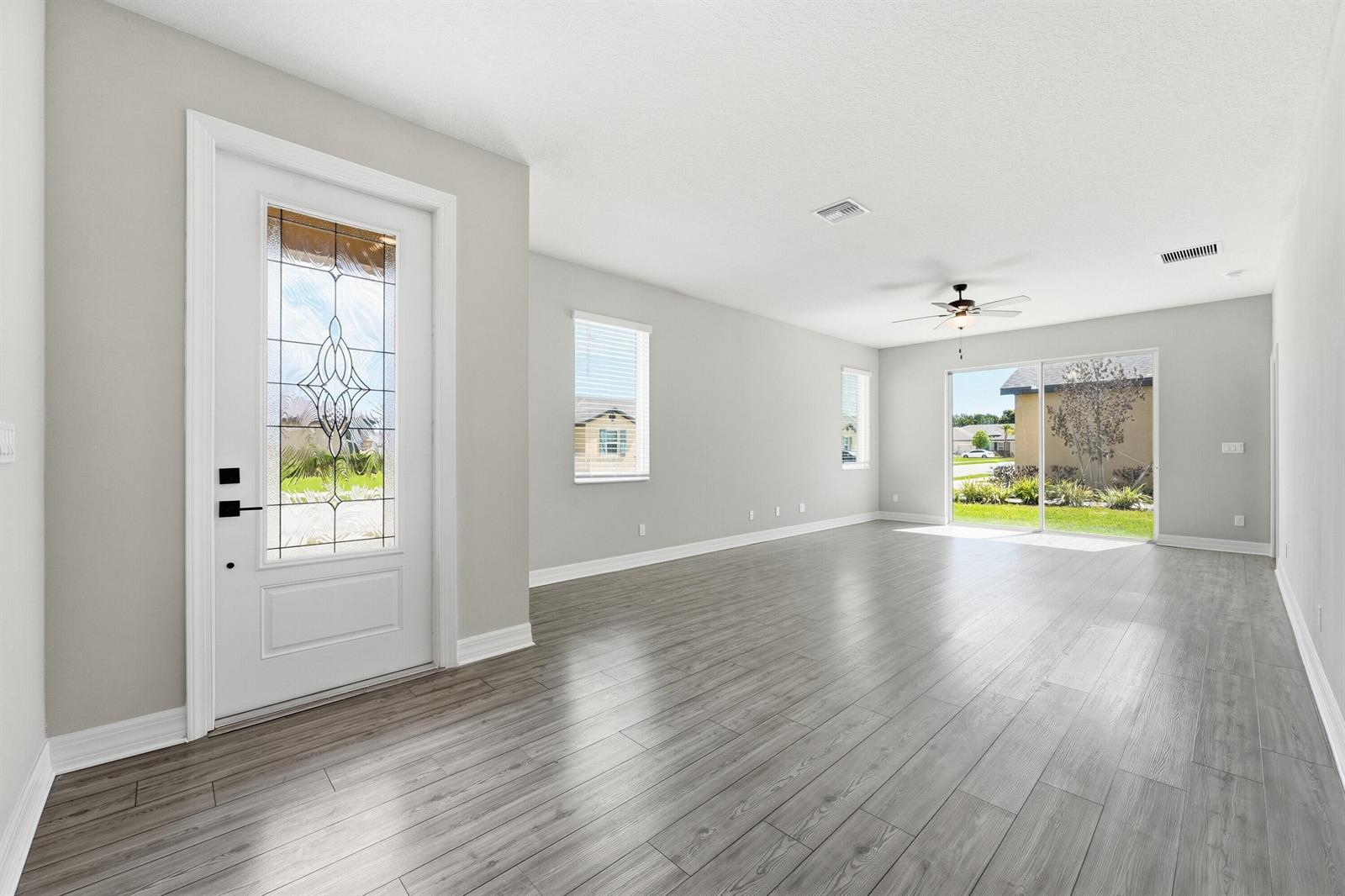 An empty living room features gray wood-look flooring, light walls, a ceiling fan, and glass doors — 1802 Celebration Drive, Fort Pierce FL 34947, FORT PIERCE, FL
