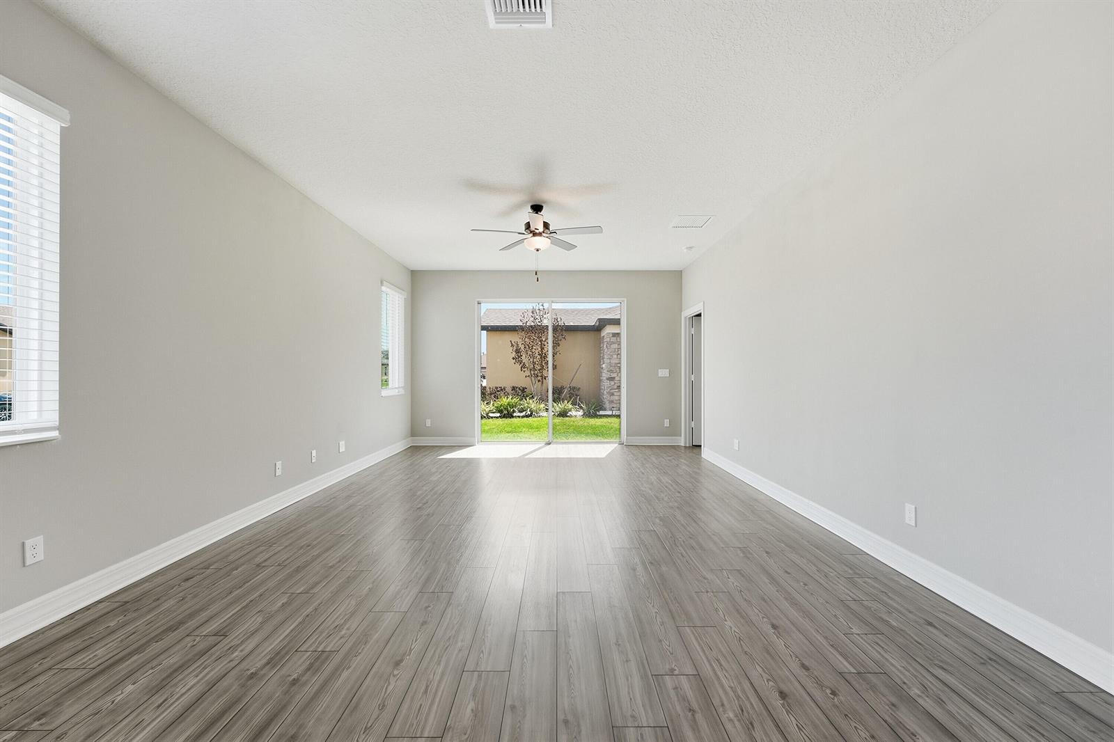 An empty living room features gray wood-look flooring, white walls, and a sliding glass door — 1802 Celebration Drive, Fort Pierce FL 34947, FORT PIERCE, FL