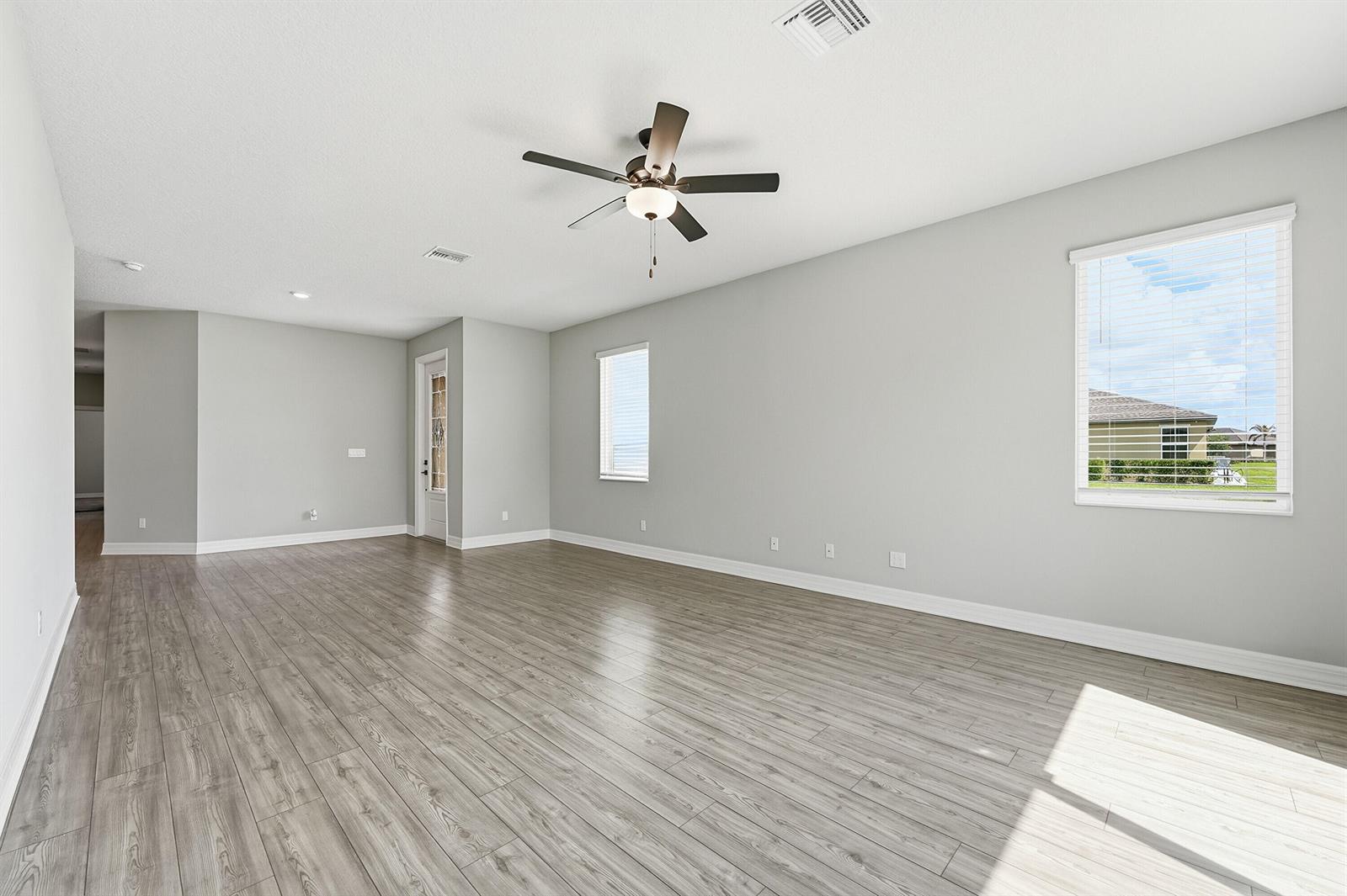 An empty living room features light gray walls, wood-look flooring, and a ceiling fan — 1802 Celebration Drive, Fort Pierce FL 34947, FORT PIERCE, FL