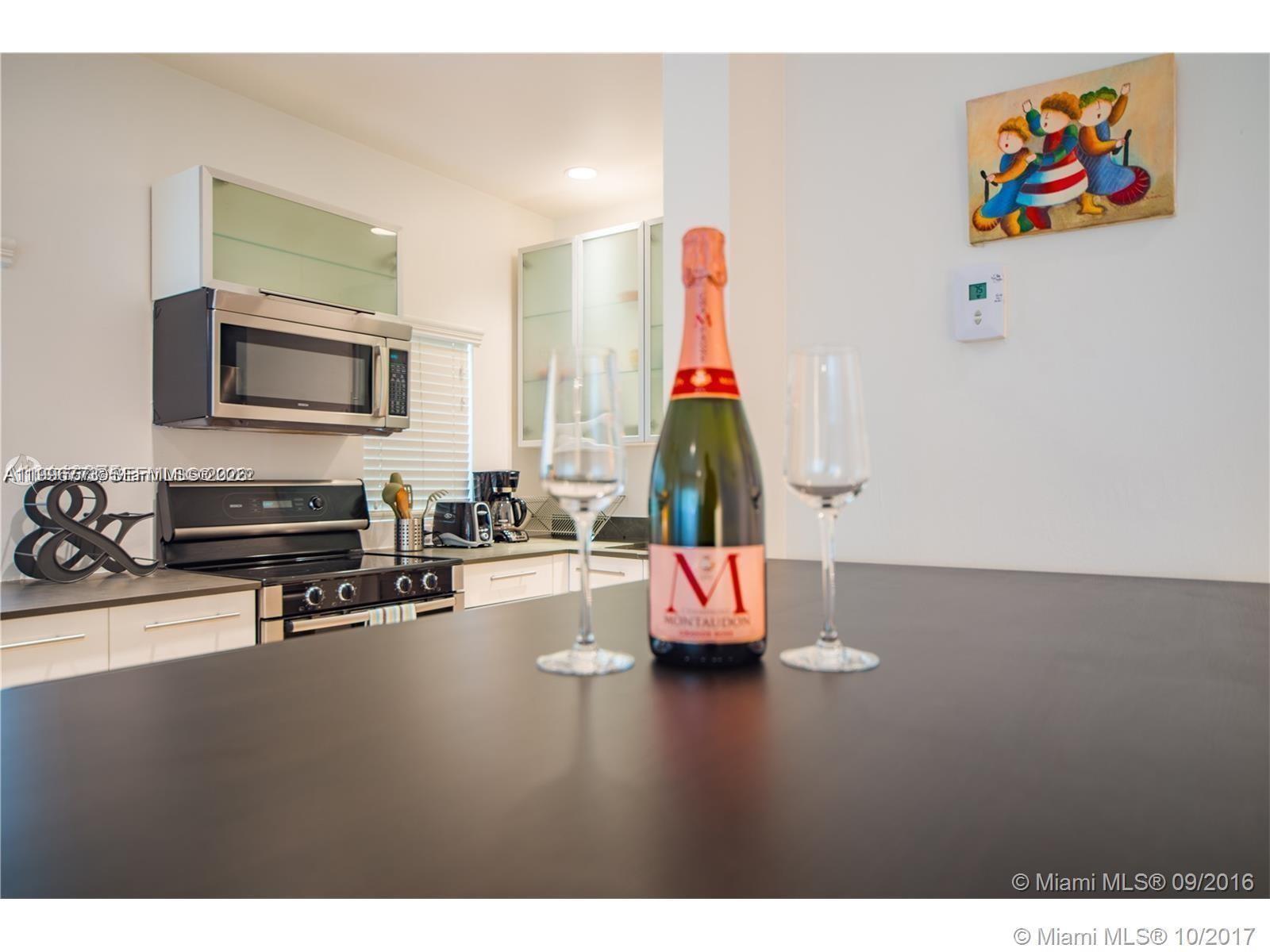 A kitchen features dark countertops, stainless steel appliances, and a bottle of champagne on display — 929 Michigan Ave # 1, Miami Beach FL 33139, MIAMI BEACH, FL
