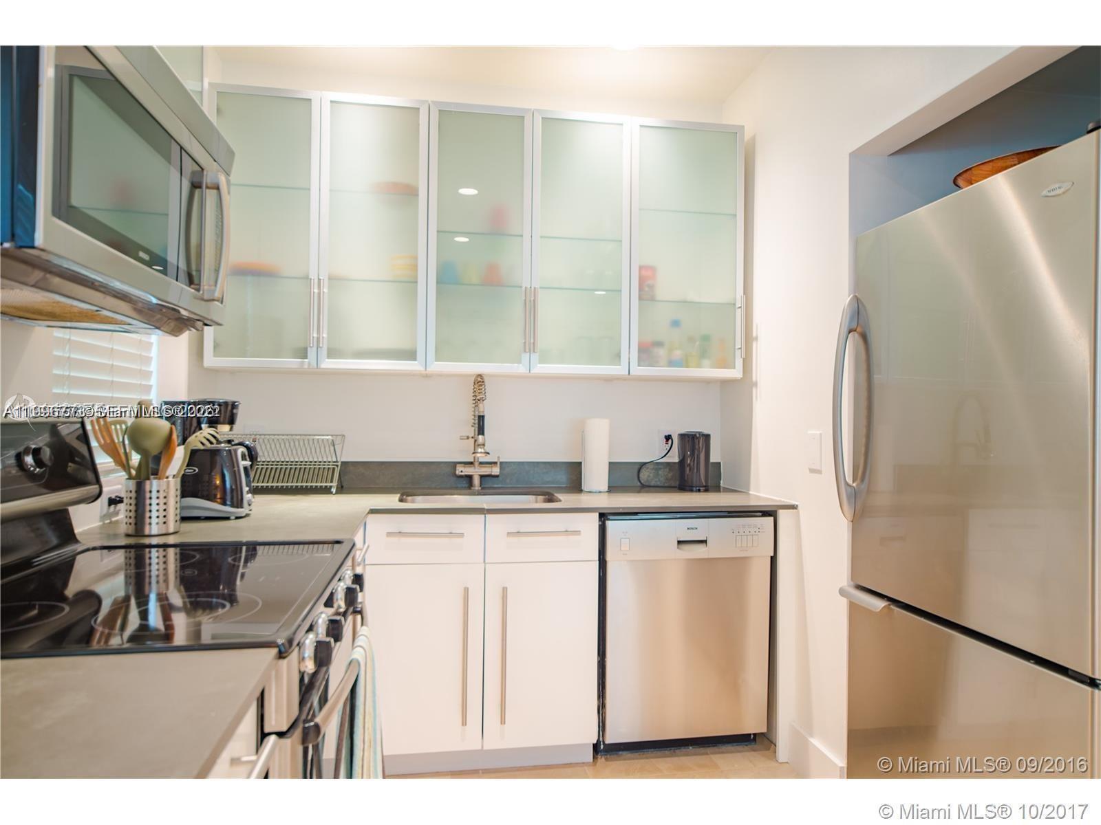 A compact kitchen features white cabinets, stainless steel appliances, and frosted glass upper cabinet doors — 929 Michigan Ave # 1, Miami Beach FL 33139, MIAMI BEACH, FL