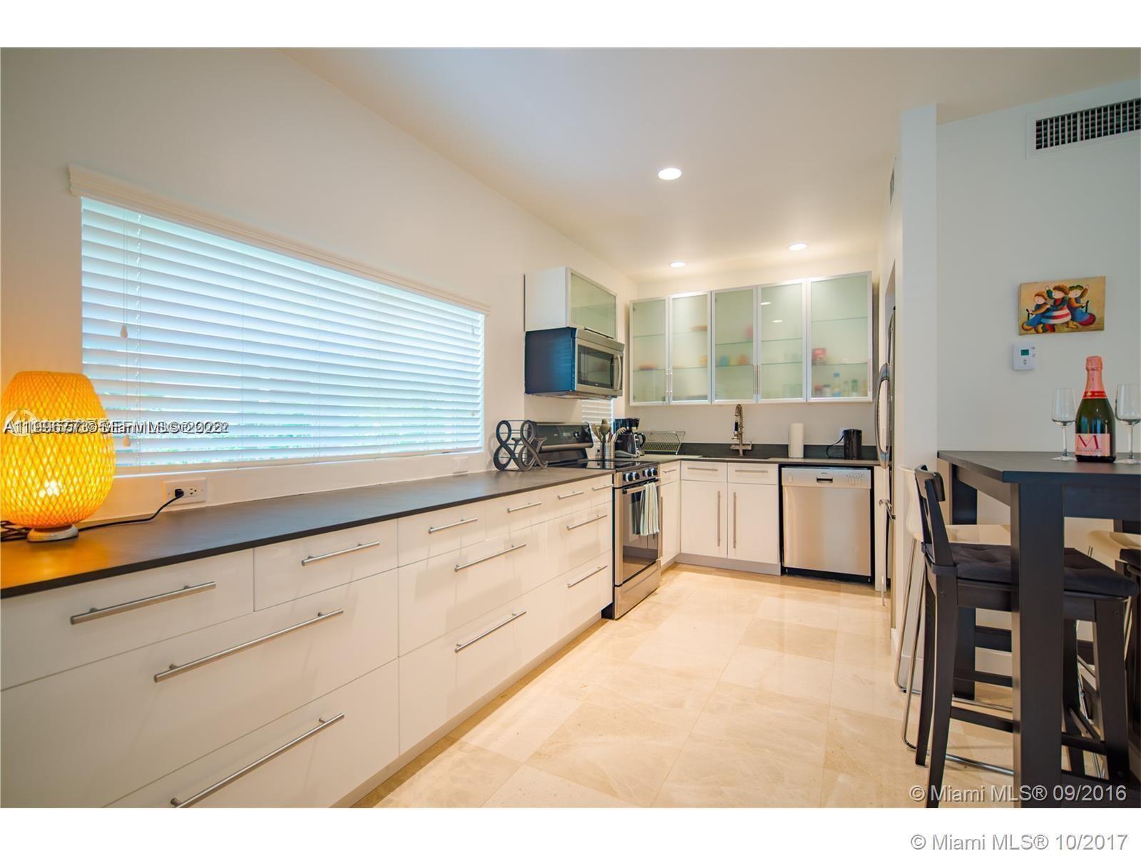 A modern kitchen features white cabinetry, stainless steel appliances, and a long black countertop — 929 Michigan Ave # 1, Miami Beach FL 33139, MIAMI BEACH, FL
