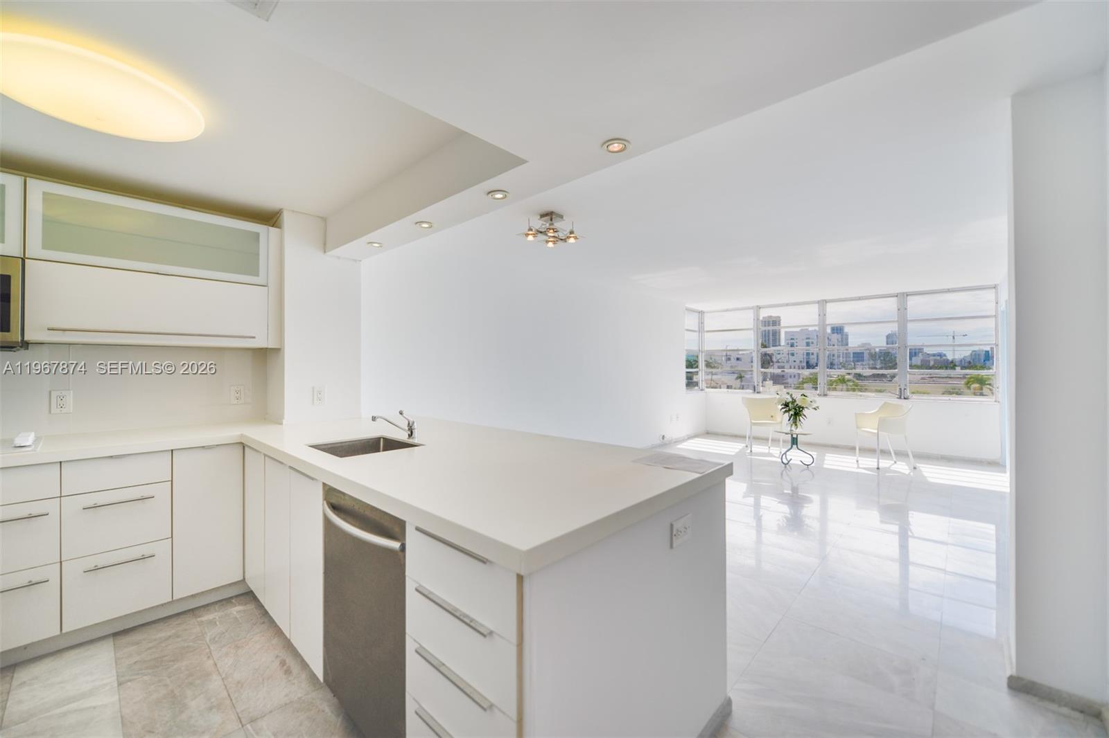 A modern white kitchen with an island overlooks a bright living area with city views — 8000 Harding Ave # 4B, Miami Beach FL 33141, MIAMI BEACH, FL