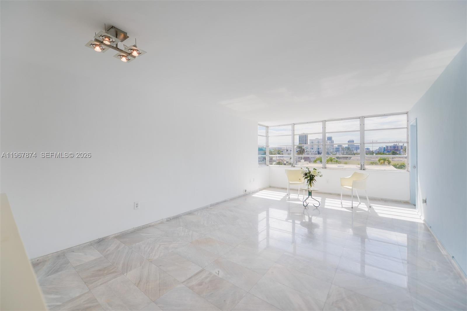 A bright, empty room features white walls, marble tile flooring, and large windows with city views — 8000 Harding Ave # 4B, Miami Beach FL 33141, MIAMI BEACH, FL