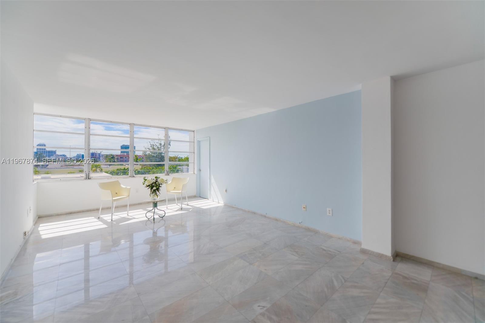 A bright, empty room features light blue walls, marble tile flooring, and large windows — 8000 Harding Ave # 4B, Miami Beach FL 33141, MIAMI BEACH, FL