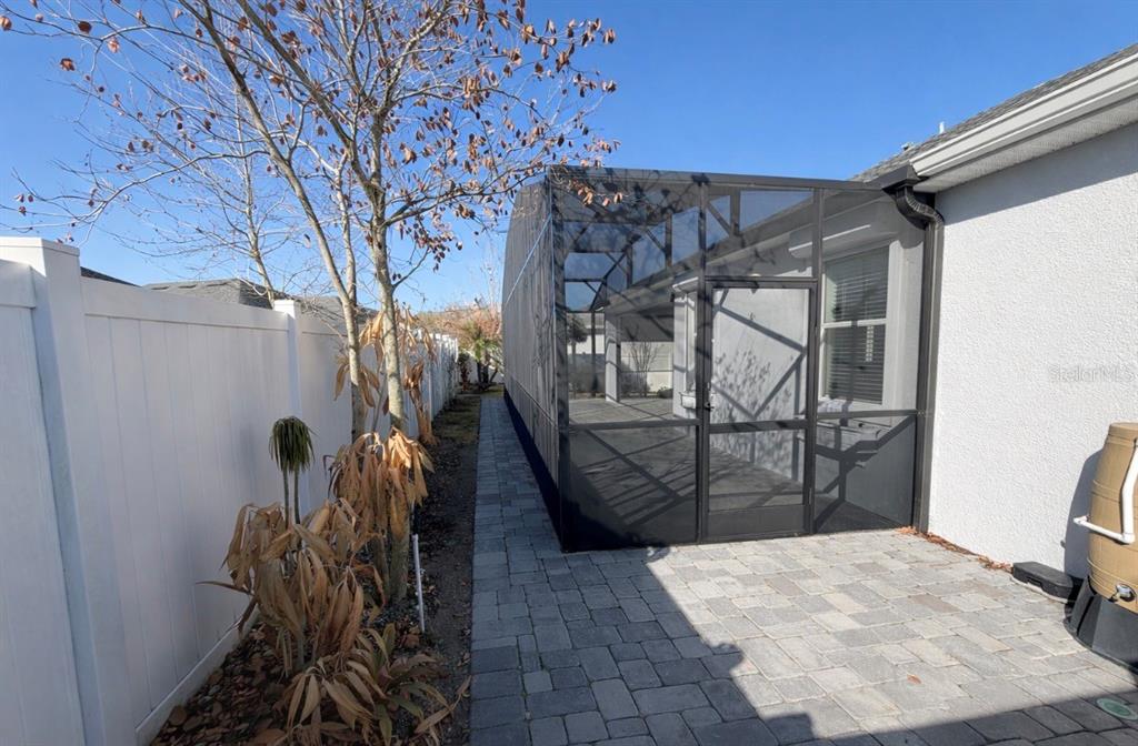 A paved walkway runs alongside a screened-in patio enclosure next to a white vinyl fence — 4638 TERRY TOWN DRIVE, KISSIMMEE, FL