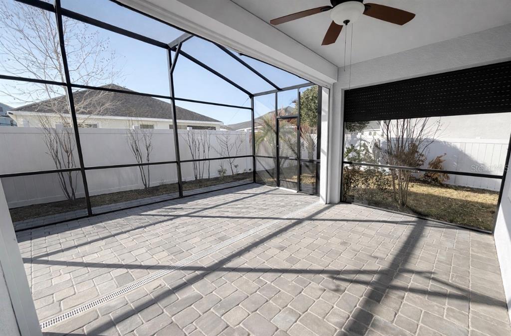 A screened-in patio with gray paver flooring, a ceiling fan, and a white privacy fence — 4638 TERRY TOWN DRIVE, KISSIMMEE, FL