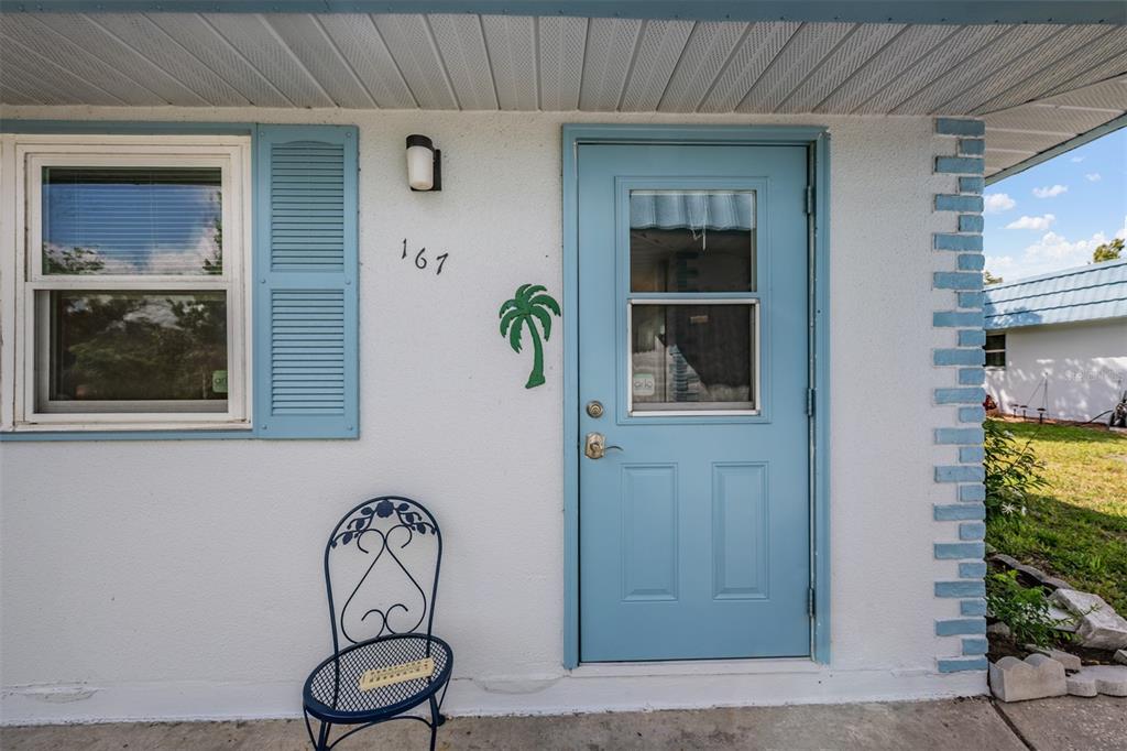 The exterior of a home features a blue door, a window with shutters, and a chair — 302 ANDOVER PLACE S UNIT 167, SUN CITY CENTER, FL