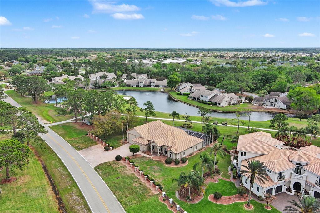 An aerial view shows a residential neighborhood with houses, a pond, and a paved road — 3114 SPRUCE CREEK BOULEVARD, PORT ORANGE, FL