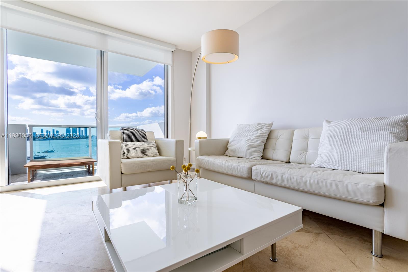 A modern living room features a white sofa, armchair, coffee table, and a balcony with water views — 1200 West Ave # 526, Miami Beach FL 33139, MIAMI BEACH, FL