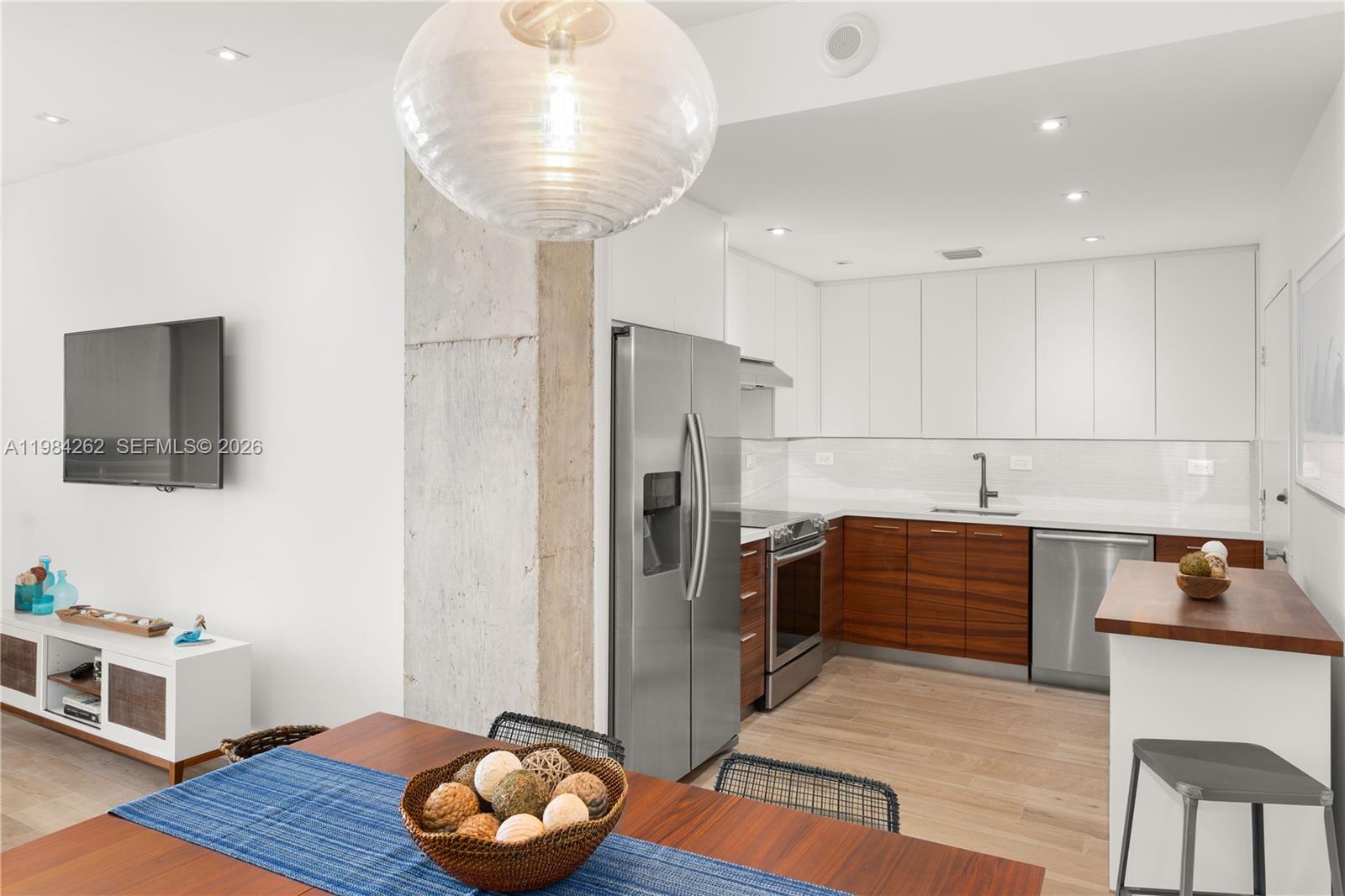 A modern kitchen features white upper cabinets, wood lower cabinets, and stainless steel appliances — 5555 Collins Ave # 17J, Miami Beach FL 33140, MIAMI BEACH, FL