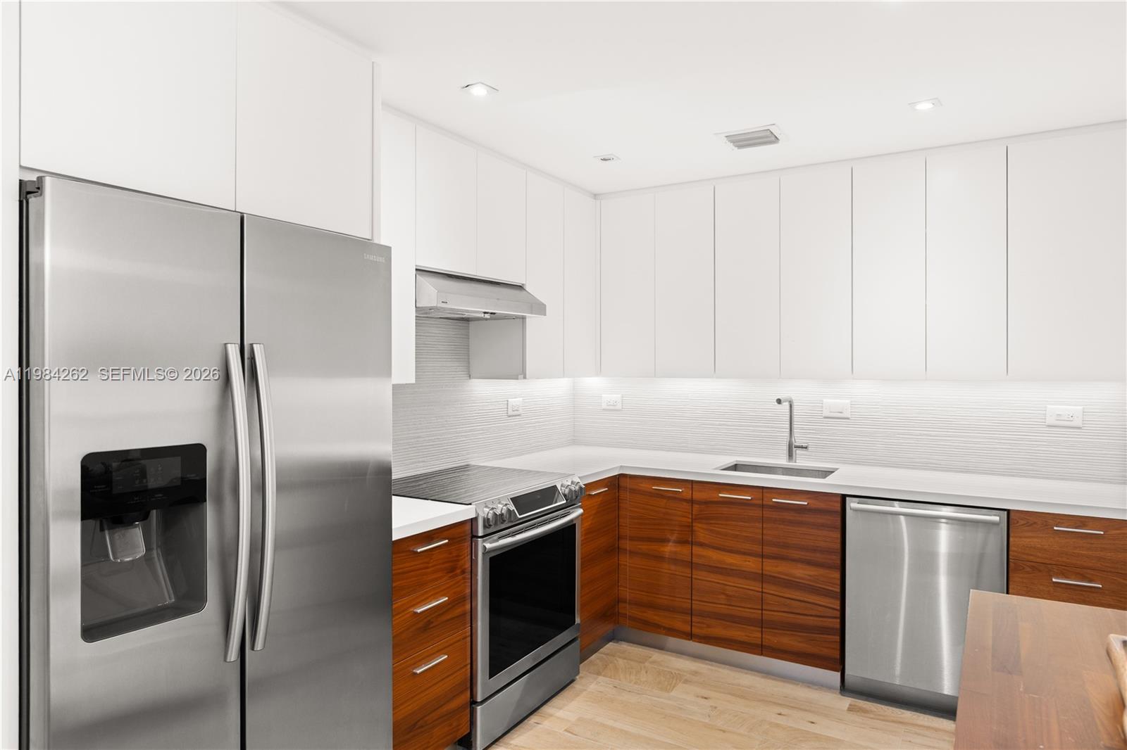 A modern kitchen features white upper cabinets, wood-grain lower cabinets, and stainless steel appliances — 5555 Collins Ave # 17J, Miami Beach FL 33140, MIAMI BEACH, FL