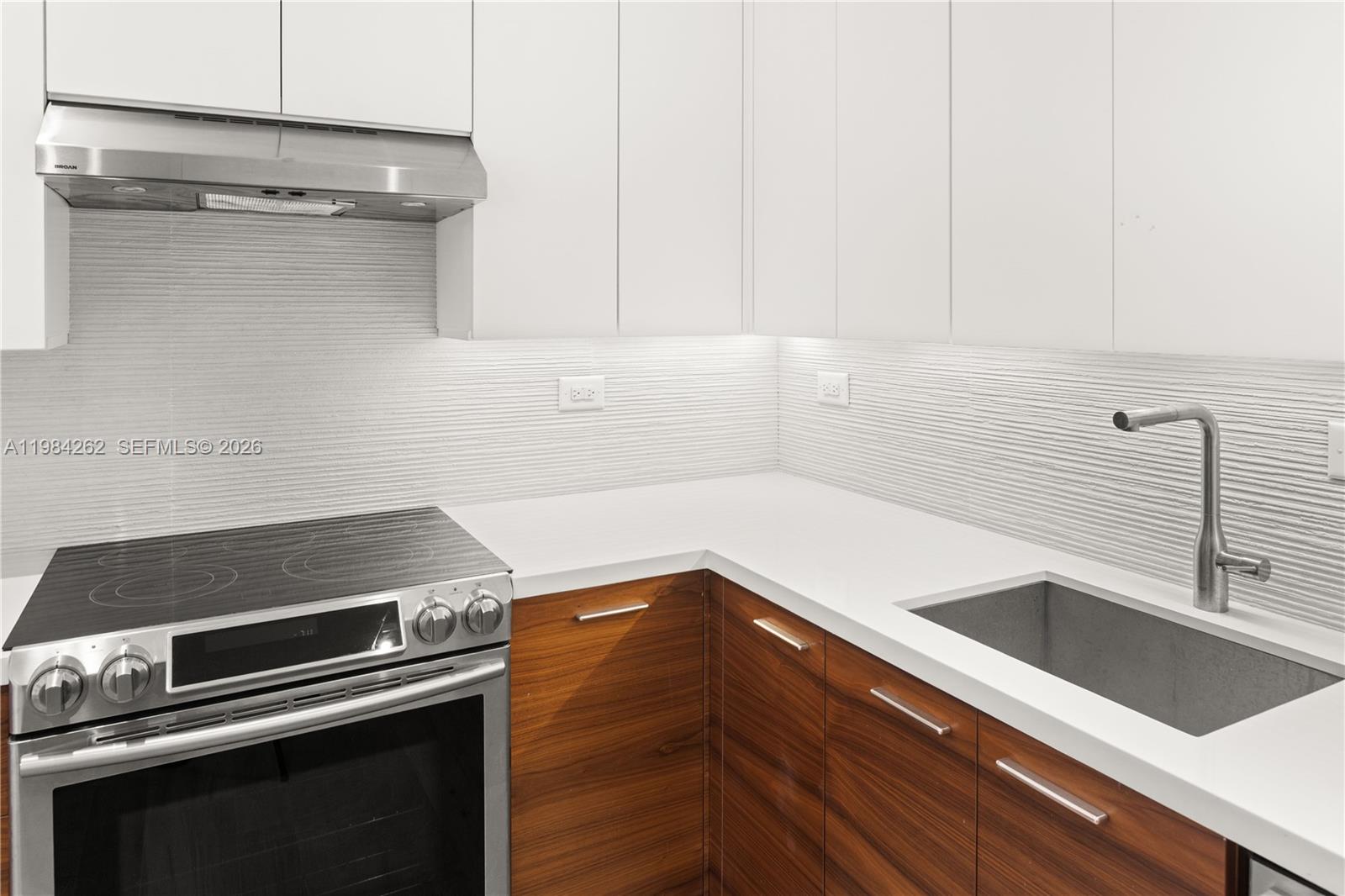 A modern kitchen features white upper cabinets, wood-grain lower cabinets, and a white countertop — 5555 Collins Ave # 17J, Miami Beach FL 33140, MIAMI BEACH, FL