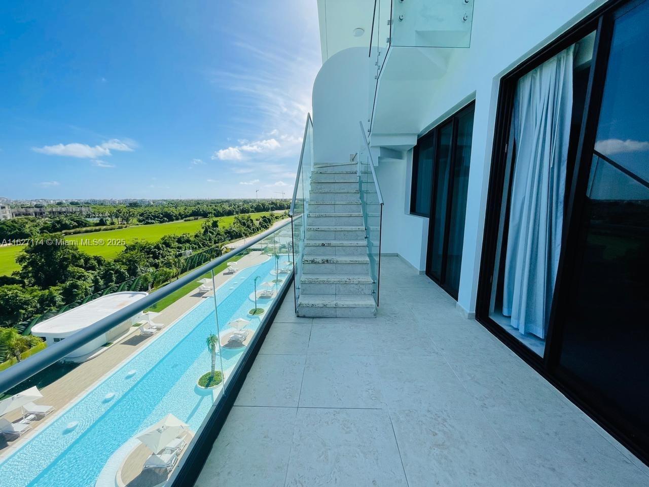 A balcony with stone flooring, glass railings, and stairs overlooking a long swimming pool — Av. Hard Rock Punta Cana 23000 #PH-510 , Dominican Republic, DR, DR