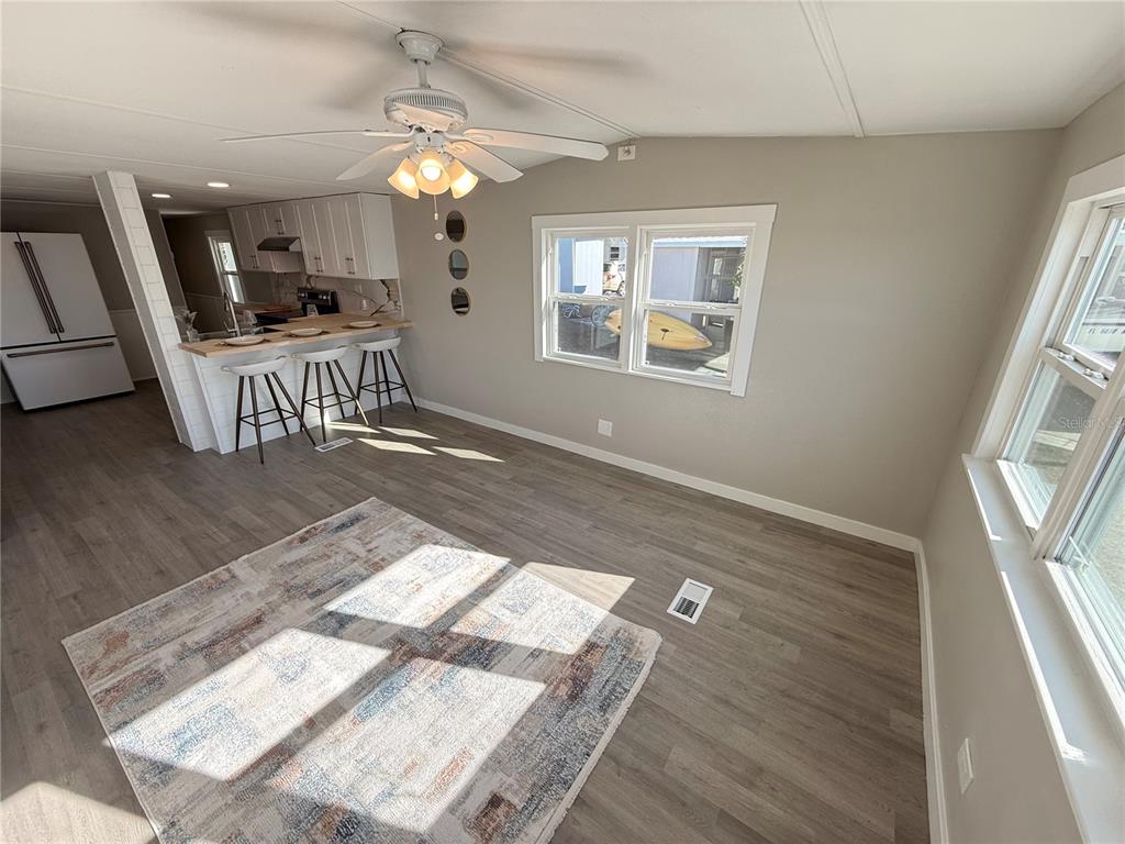 A living room with light wood flooring, a ceiling fan, and an open kitchen area — 1800 ENGLEWOOD ROAD UNIT 136, ENGLEWOOD, FL