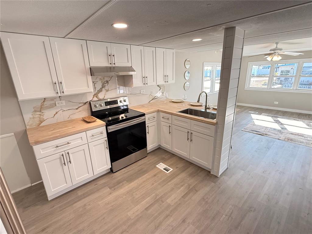 A kitchen features white cabinets, butcher block countertops, a stainless steel stove, and wood flooring — 1800 ENGLEWOOD ROAD UNIT 136, ENGLEWOOD, FL