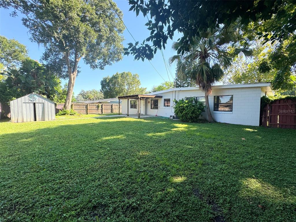 A backyard view of a white concrete block house with a shed and lawn — 3628 DAGON STREET, ORLANDO, FL