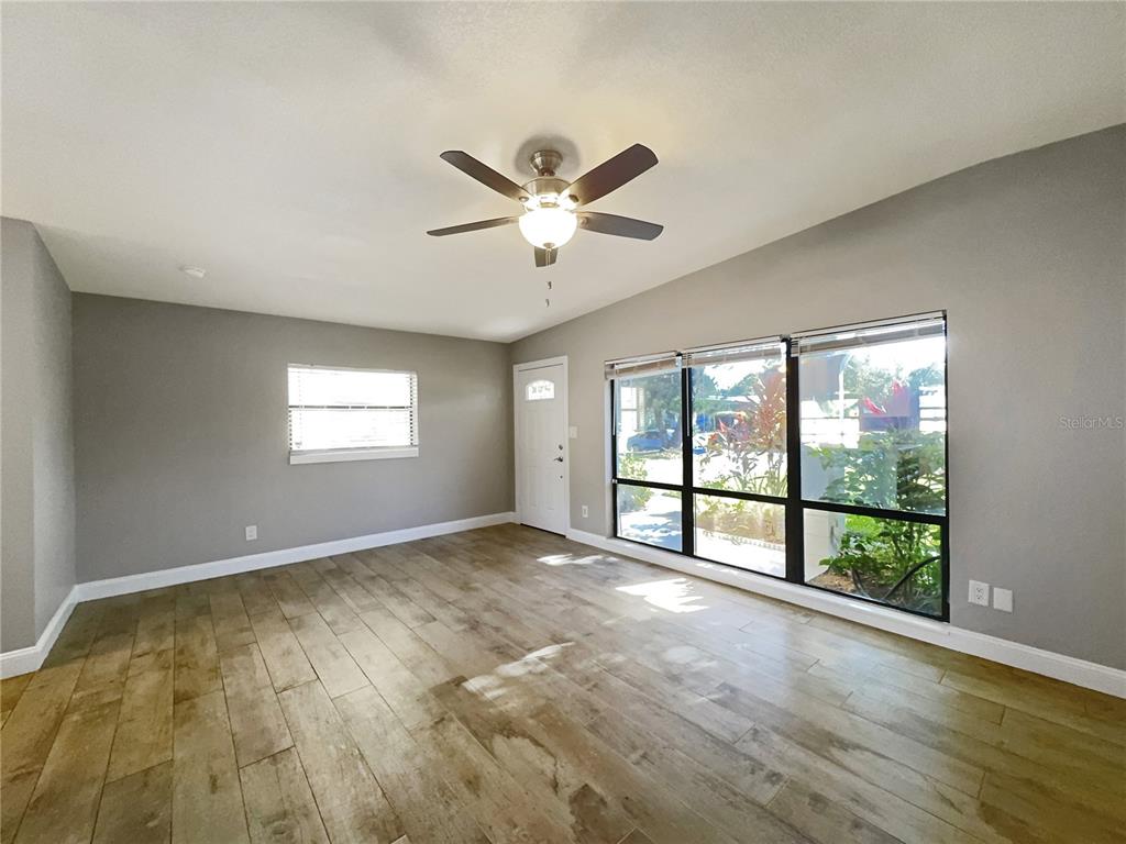 An empty living room features gray walls, wood-look tile flooring, a ceiling fan, and large windows — 3628 DAGON STREET, ORLANDO, FL