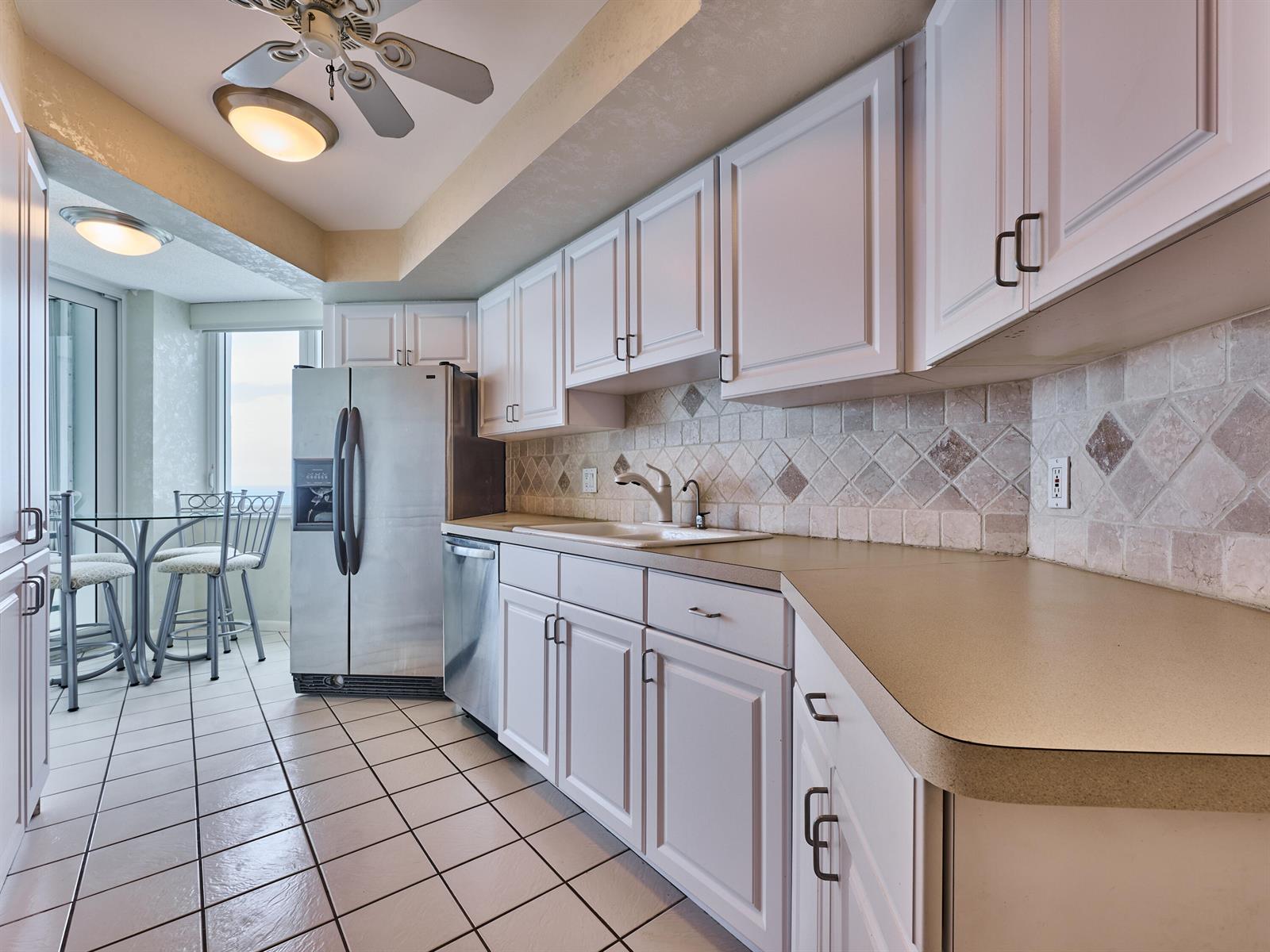 A kitchen features white cabinets, stainless steel appliances, a tiled backsplash, and a dining area — 500 S Ocean Boulevard # 2106, Boca Raton FL 33432, BOCA RATON, FL