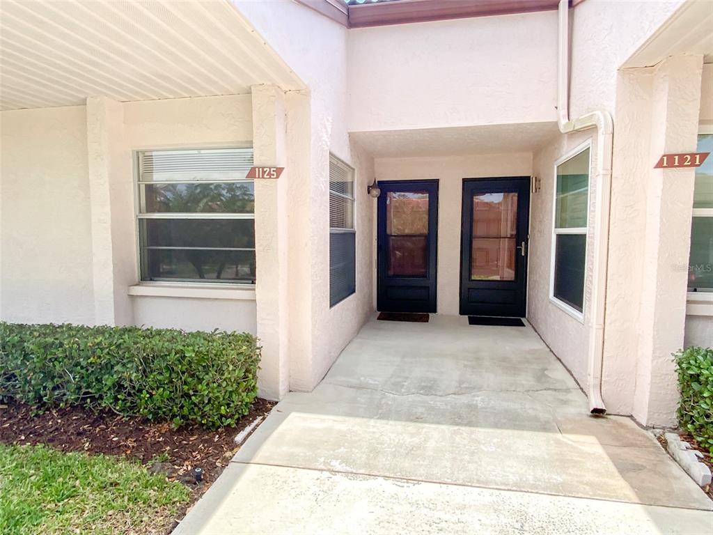The exterior view shows two adjacent black front doors with house numbers 1125 and 1121 — 1125 MONTROSE PLACE, DUNEDIN, FL