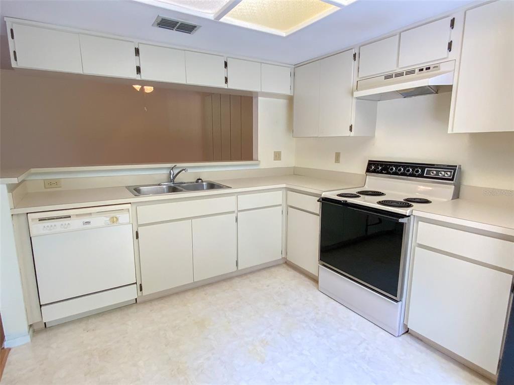A kitchen features white cabinets, a double sink, a dishwasher, and a freestanding electric stove — 1125 MONTROSE PLACE, DUNEDIN, FL
