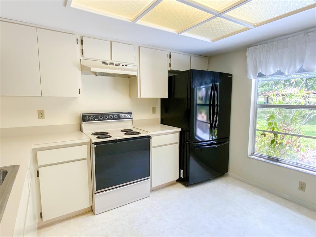 A kitchen features white cabinets, a black refrigerator, a white stove, and a window — 1125 MONTROSE PLACE, DUNEDIN, FL