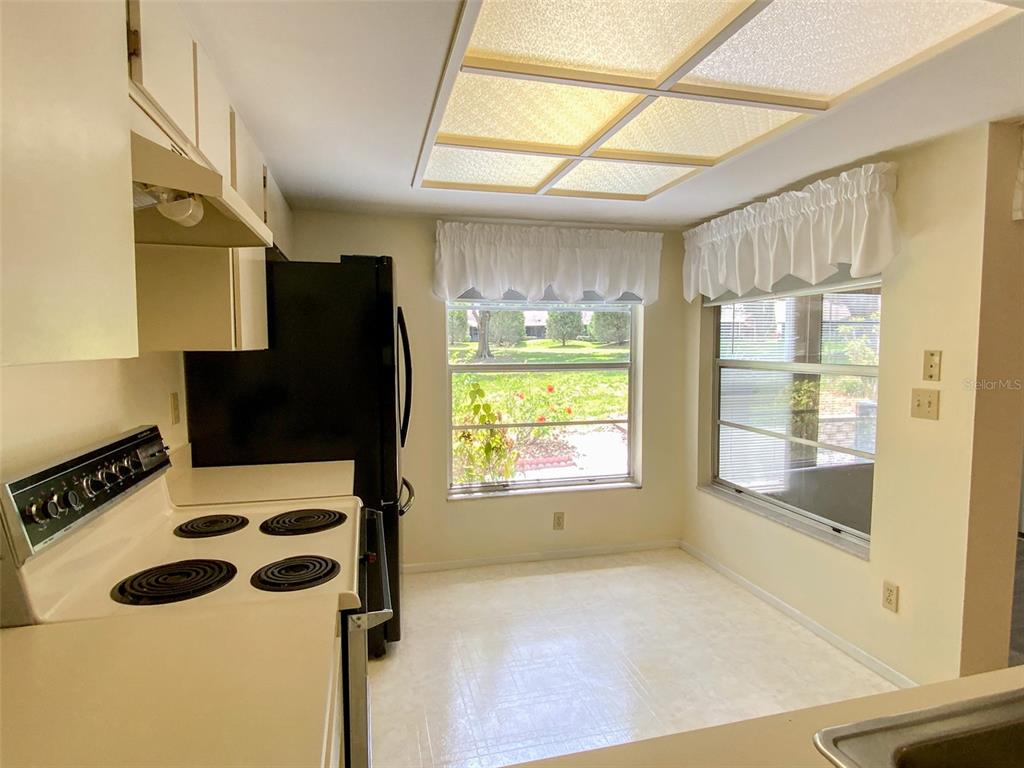 A kitchen with white cabinets, a black refrigerator, an electric stove, and a dining area — 1125 MONTROSE PLACE, DUNEDIN, FL