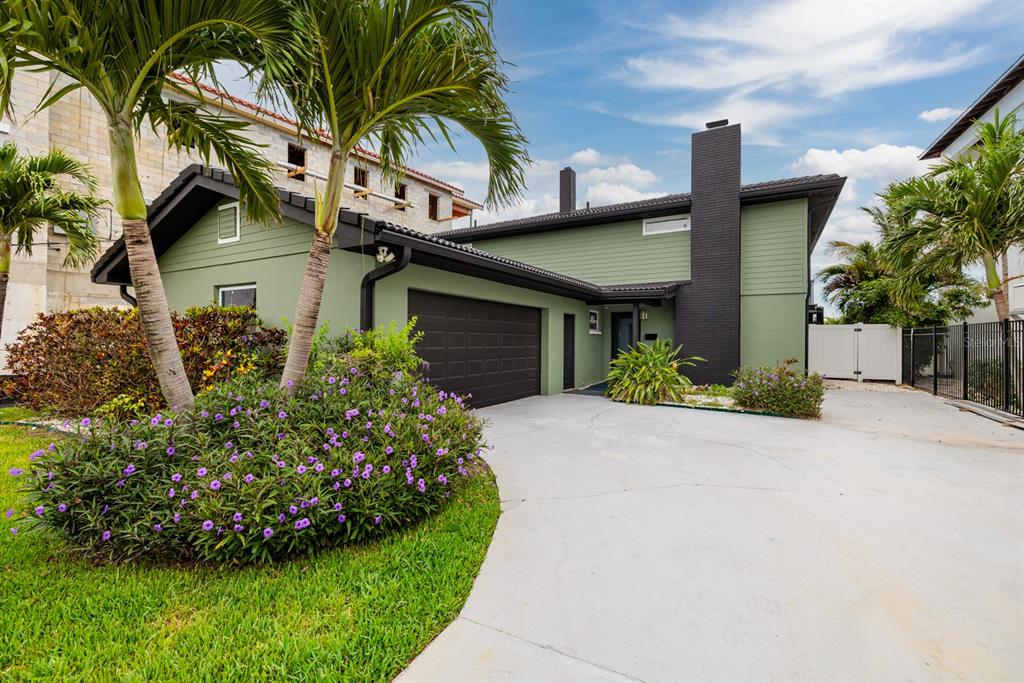 A green house with a black chimney and garage sits behind a purple-flowered garden — 3319 BAYSHORE BOULEVARD NE, ST PETERSBURG, FL