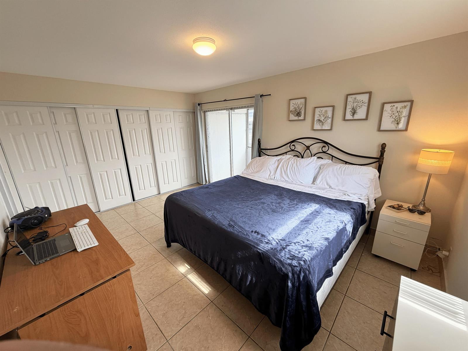 A bedroom features a bed with a dark blue cover, tile flooring, and closet doors — 419 Brittany Drive, Delray Beach FL 33446, DELRAY BEACH, FL