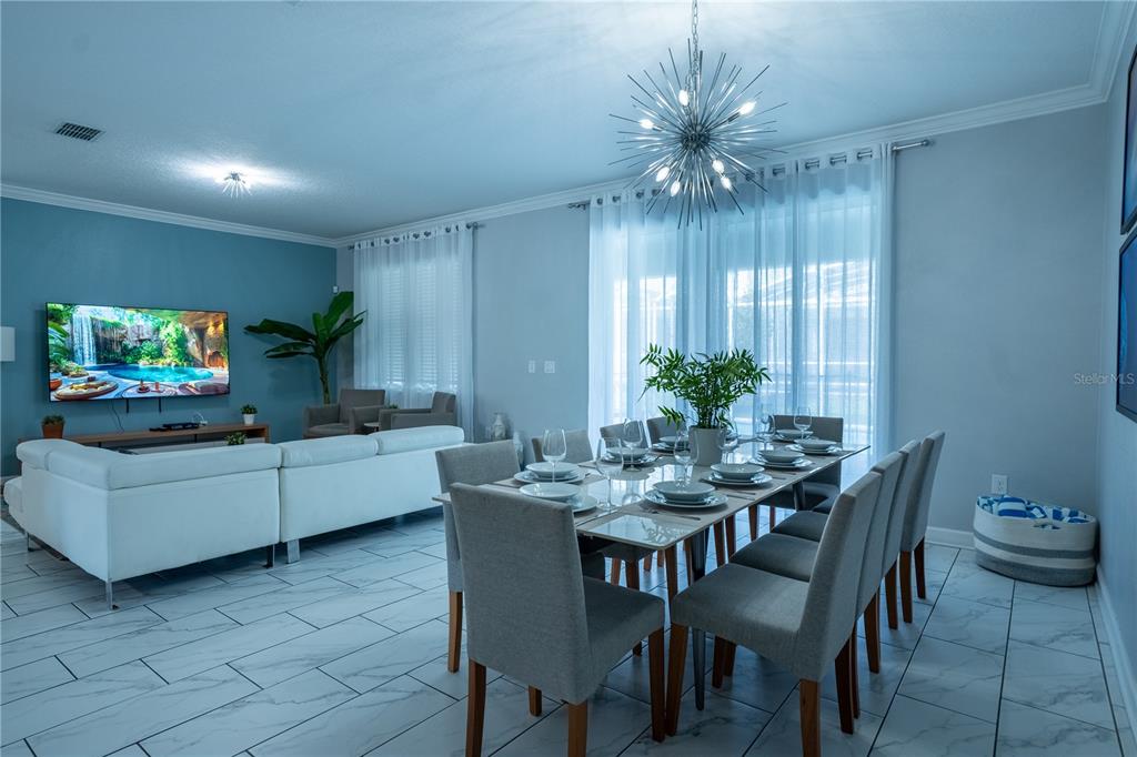 A dining area with a modern chandelier sits adjacent to a living room with tile floors — 760 DROP SHOT DRIVE, DAVENPORT, FL