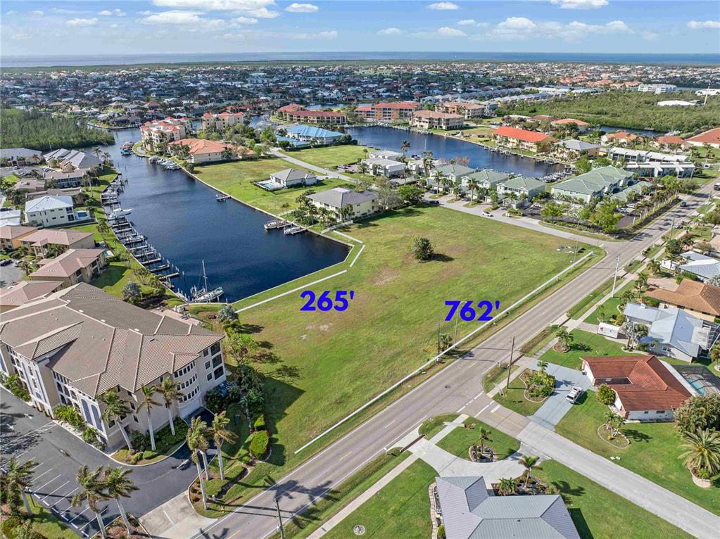 An aerial view shows a vacant grassy lot bordered by a canal and a road — 1359 AQUI ESTA DRIVE, PUNTA GORDA, FL