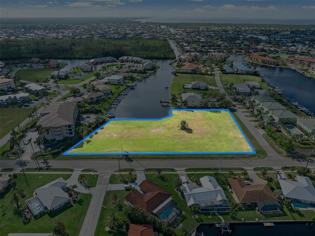 An aerial view shows a vacant, grassy lot outlined in blue next to a canal — 1359 AQUI ESTA DRIVE, PUNTA GORDA, FL