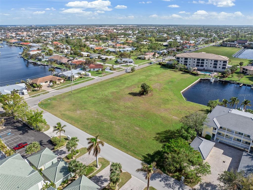 An aerial view shows a large, vacant grassy lot bordered by roads, water, and buildings — 1359 AQUI ESTA DRIVE, PUNTA GORDA, FL