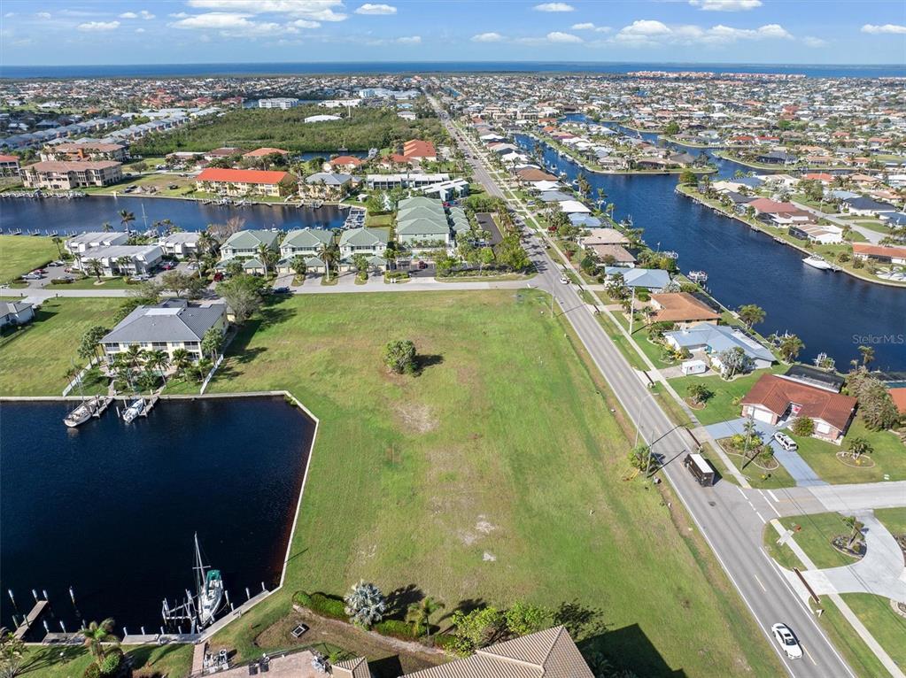 An aerial view shows a vacant grassy lot situated between a canal and a road — 1359 AQUI ESTA DRIVE, PUNTA GORDA, FL