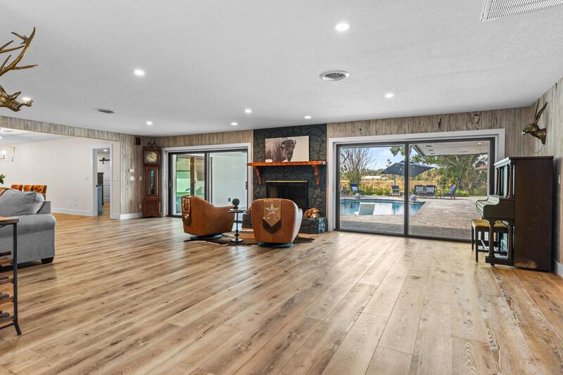 A living room features wood-look flooring, a stone fireplace, and sliding doors overlooking a pool — VERO BEACH, FL