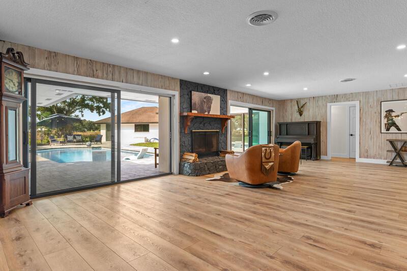 A living room features wood-look flooring, a stone fireplace, and sliding glass doors to a pool — VERO BEACH, FL