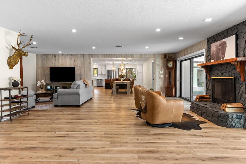 A spacious living room features wood-look flooring, a stone fireplace, and a view into the kitchen — VERO BEACH, FL