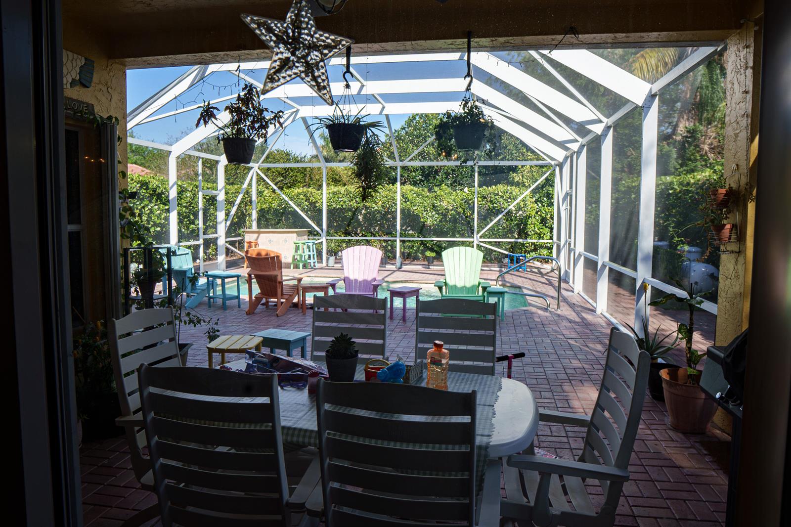 A screened-in patio features a dining set, colorful lounge chairs, and a swimming pool — 8058 Via Hacienda, Riviera Beach FL 33418, RIVIERA BEACH, FL